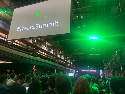 Foto van een publiek kijkend naar schermen met daarop het logo van React Summit